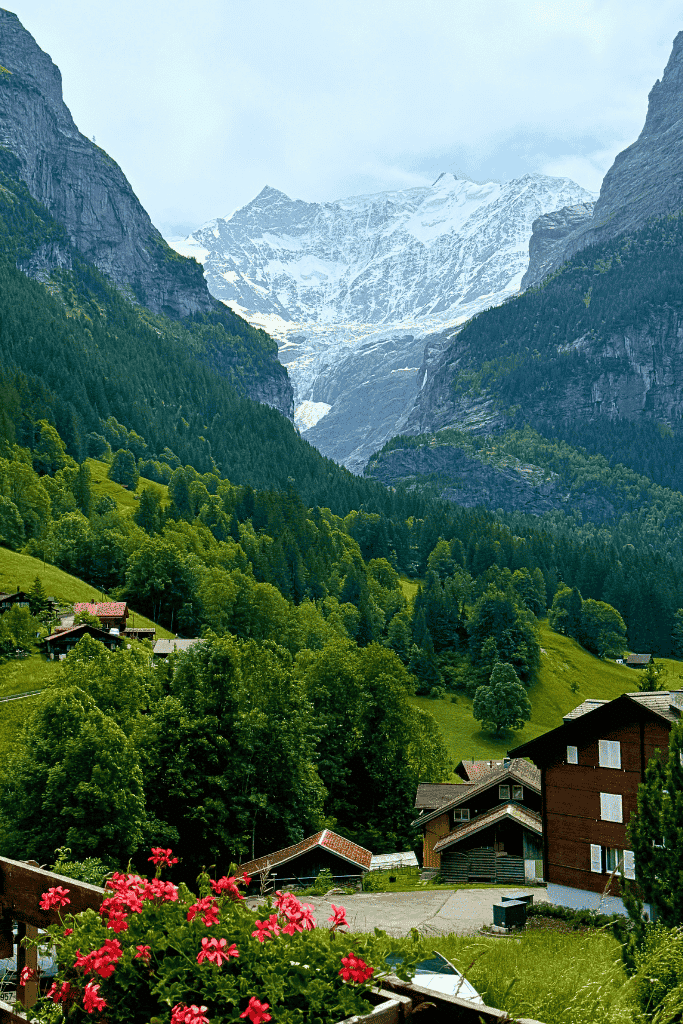 Charming alpine chalets in Grindelwald sit nestled among green hills, with towering snow-covered mountains rising dramatically in the distance.