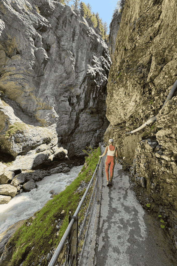 Kate walks along a narrow path carved into a rock canyon in Grindelwald, following a rushing river through the dramatic ravine.