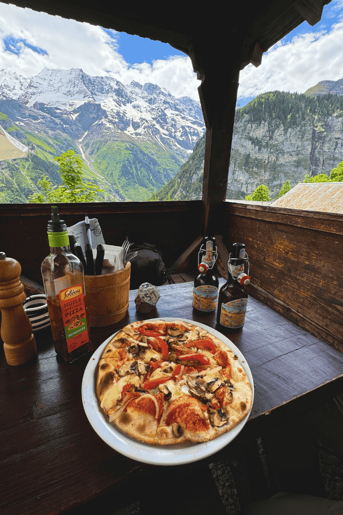 A peaceful view over the alpine village of Gimmelwald, with rustic red-roofed buildings nestled beneath steep cliffs and dramatic snowy mountains.