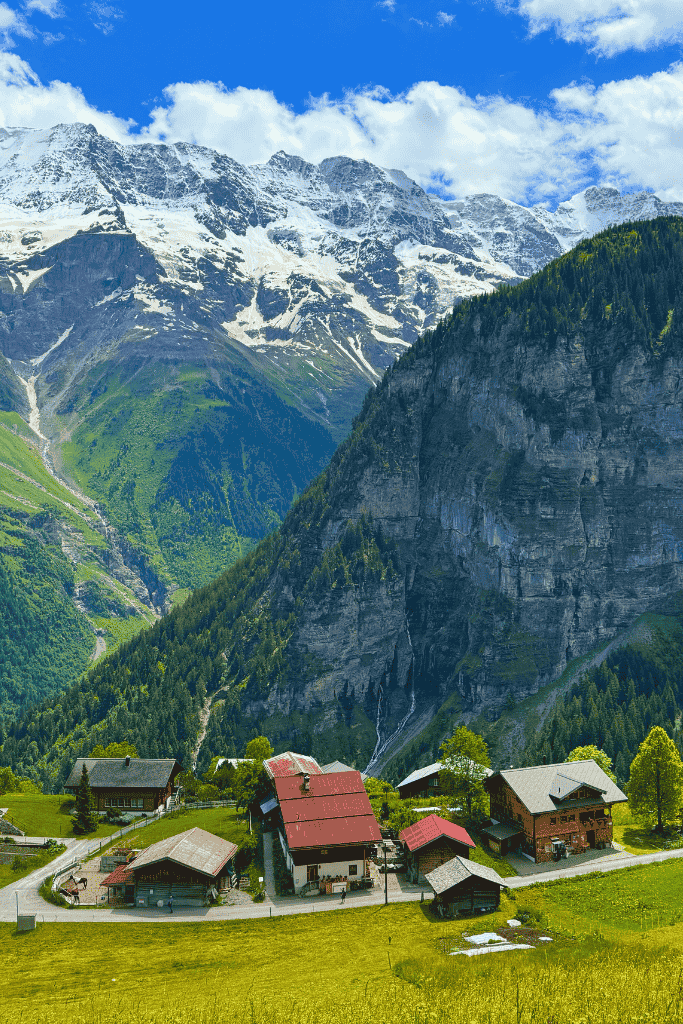 A fresh pizza and beers sit on a wooden table at a balcony restaurant in Gimmelwald, with stunning views of the Swiss Alps in the background.