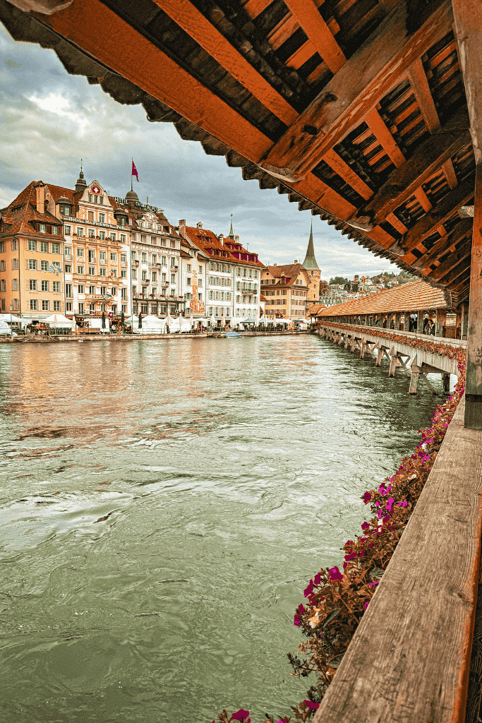 View of the Reuss River and historic buildings in Lucerne, Switzerland, framed by the wooden roof of the iconic Chapel Bridge.