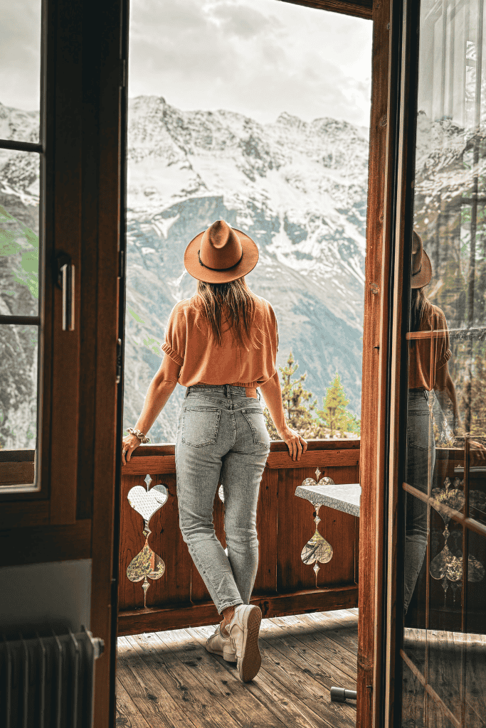 Kate leans on a wooden balcony railing, gazing out at the dramatic snow-covered peaks surrounding Mürren, Switzerland.