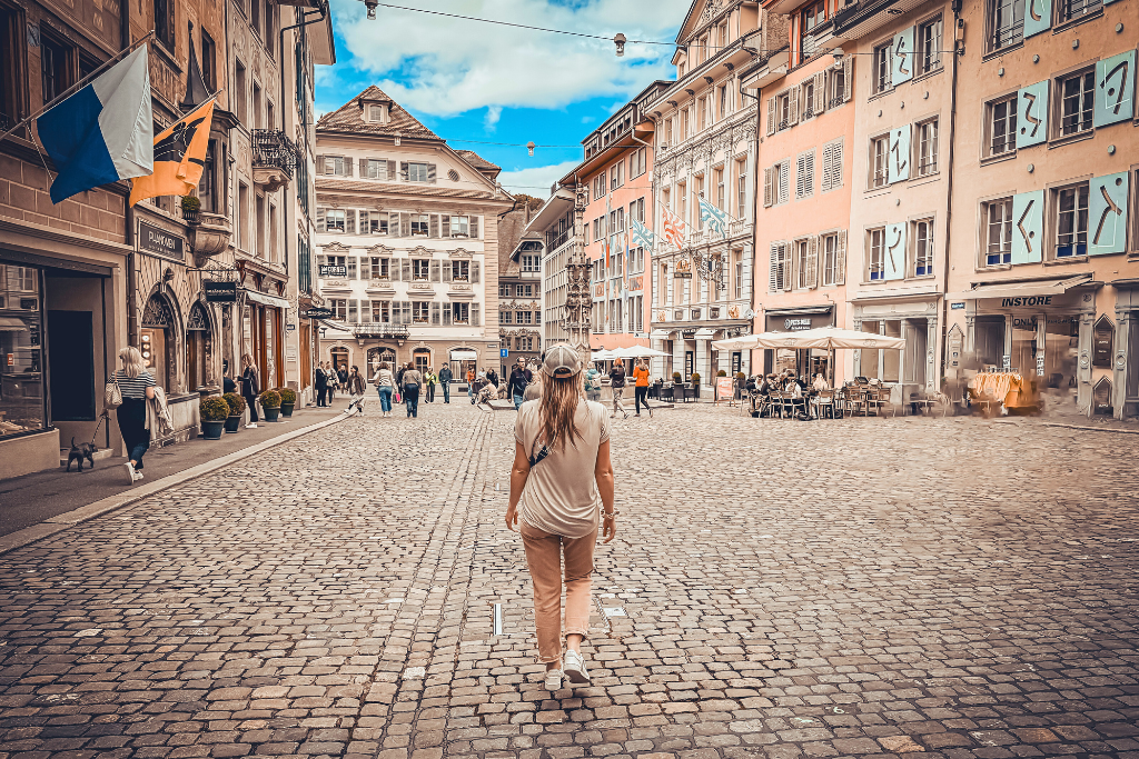Kate walking down a cobble stone street in Lucerne Switzerland wearing a ball cap, t-shirt and pink pants.