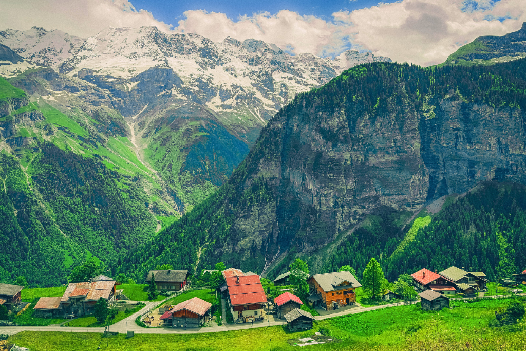 View overlooking a small mountain village in Switzerland with lush green meadows and jagged peaks in the distance. 