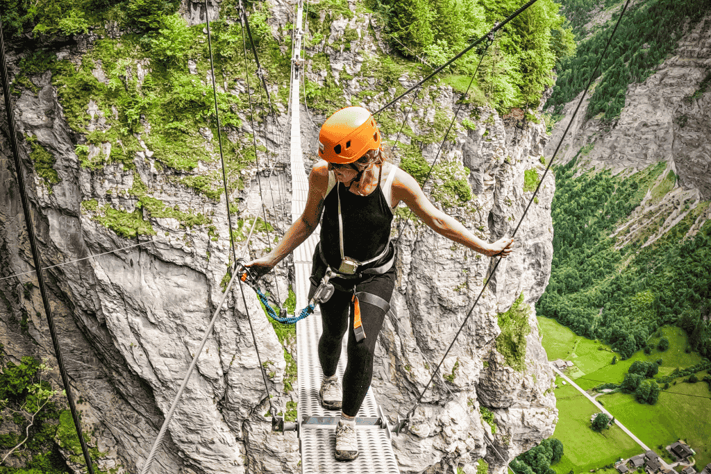 Kate carefully crosses a narrow suspension bridge in the Swiss Alps wearing a helmet and harness above a dramatic green valley in Switzerland.