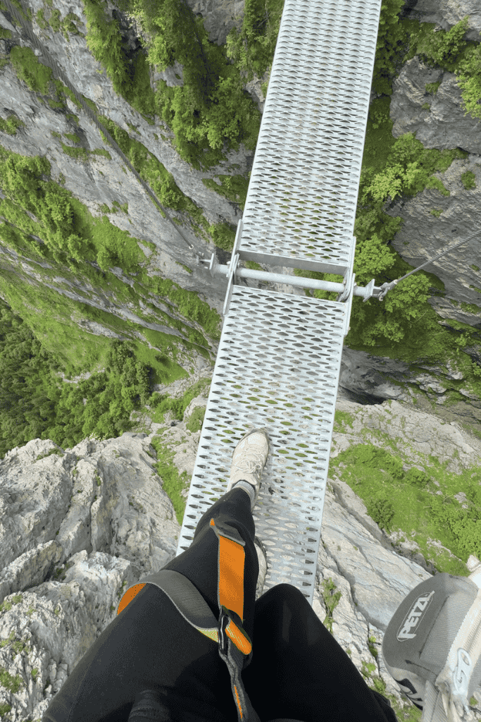 A climber’s view shows a narrow metal suspension bridge bolted into a sheer Swiss cliff with a dramatic drop into the valley beneath.