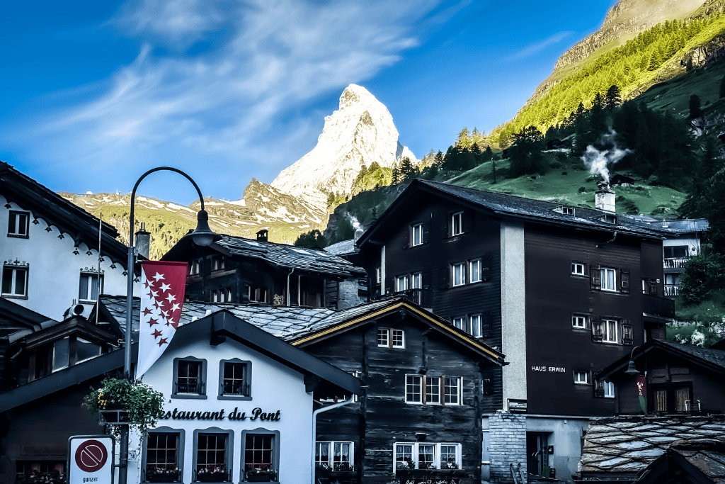 Traditional wooden chalets and a Swiss flag sit beneath the Matterhorn rising above the alpine village of Zermatt in Switzerland.