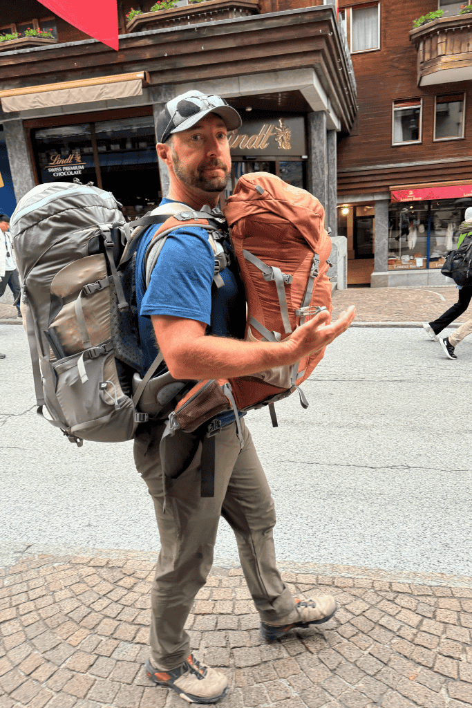 Kate’s husband walks through a Swiss town carrying large backpacks, ready for a budget friendly Switzerland adventure.