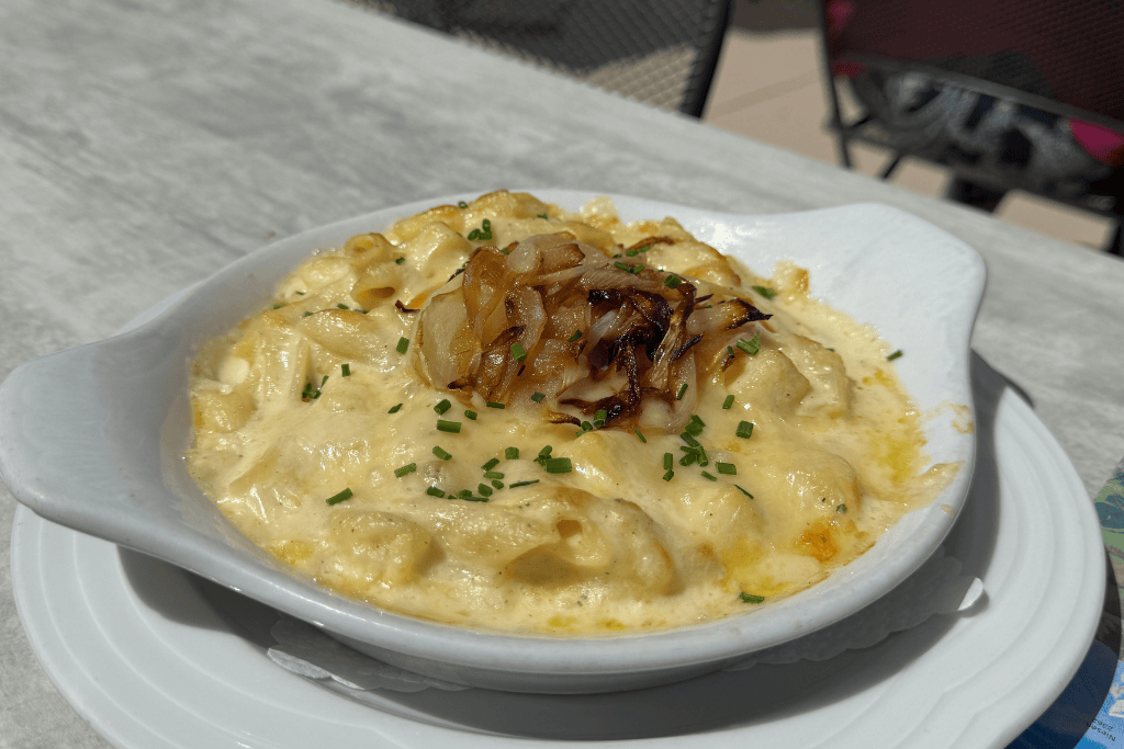 A bubbling dish of creamy Swiss macaroni and cheese topped with caramelized onions sits on an outdoor table in Switzerland.