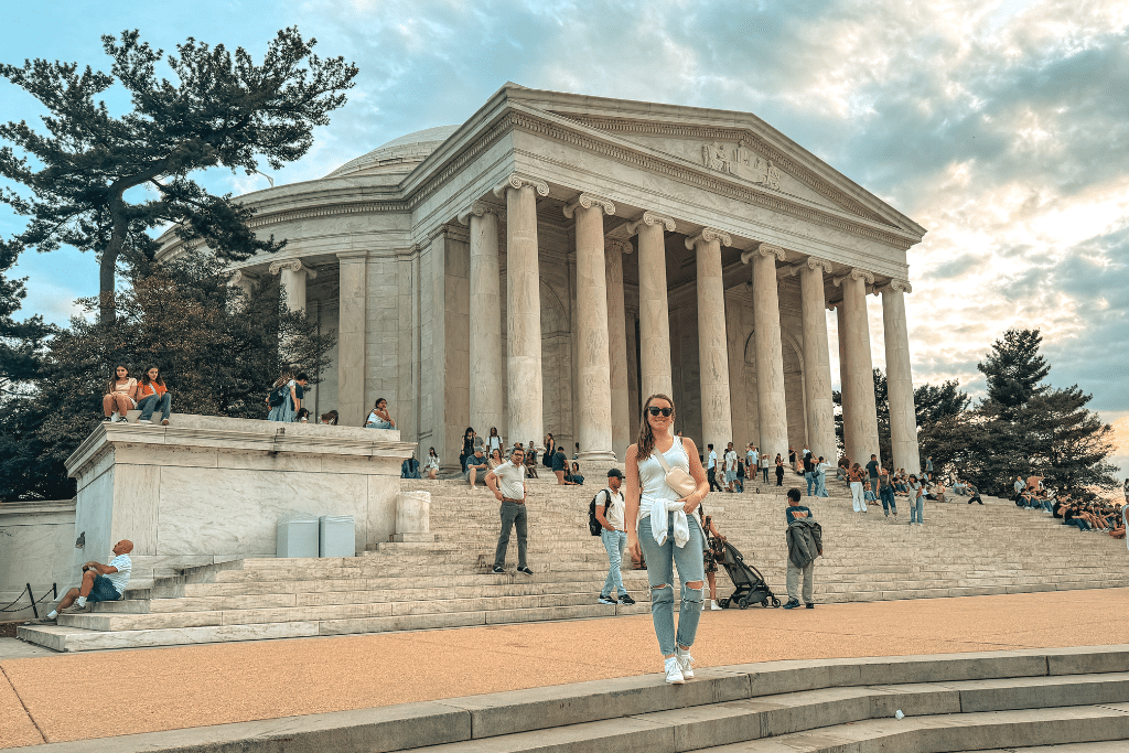 Kate smiles while standing in front of the Jefferson Memorial in Washington DC as visitors gather on the steps during a busy sightseeing day in the city.