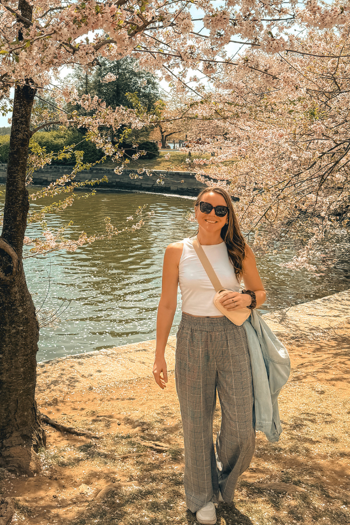 Kate stands by the water surrounded by cherry blossom trees in full bloom at Tidal Basin in Washington DC.