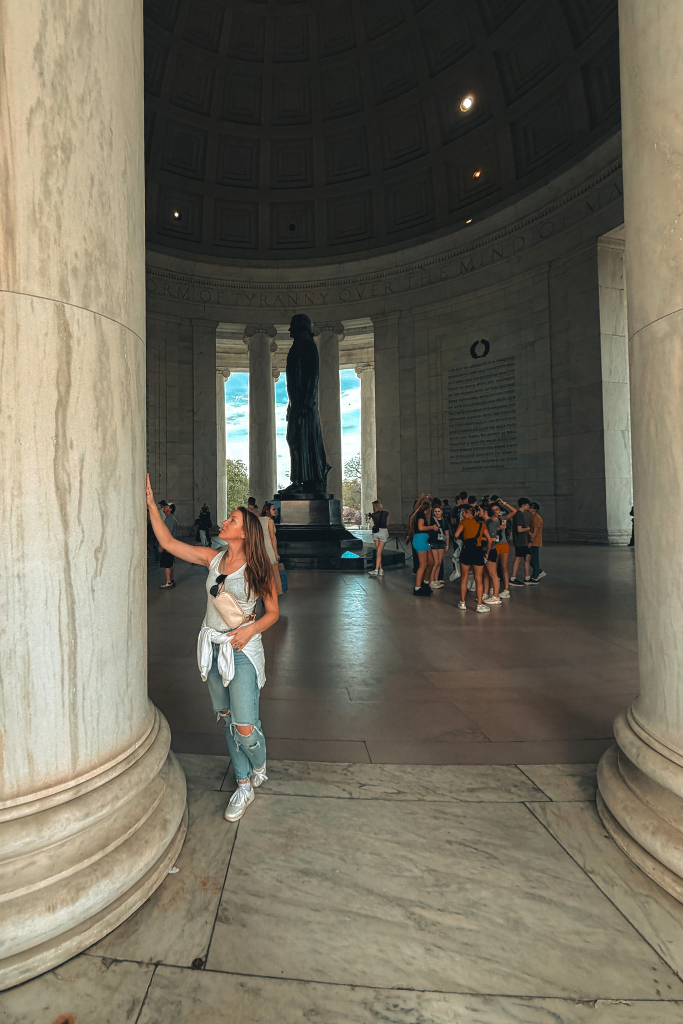 Kate stands between tall marble columns inside the Jefferson Memorial while looking up at the architecture.