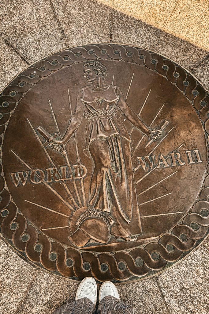 Bronze medallion on the ground in Washington DC engraved with a figure and the words "World War II" as Kate stands above it during a walk through the memorial area.