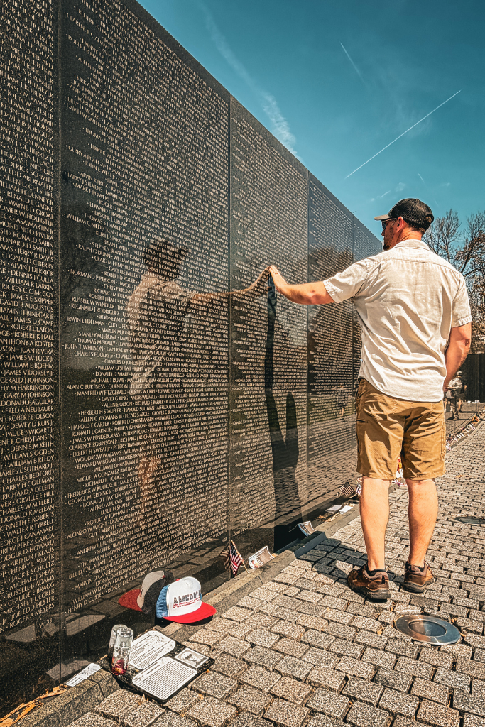 Kates husband touches the Vietnam Veterans Memorial wall in Washington DC with his reflection shown on the black wall.