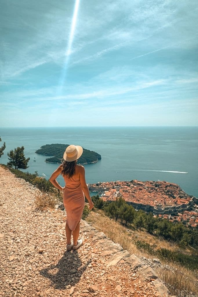 Kate standing on a rocky trail looking out over the walled city of Dubrovnik and the sea below.