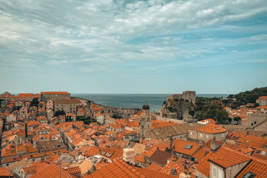 A sunny view over Dubrovnik and its orange roofs and walls with the sea in the distance.
