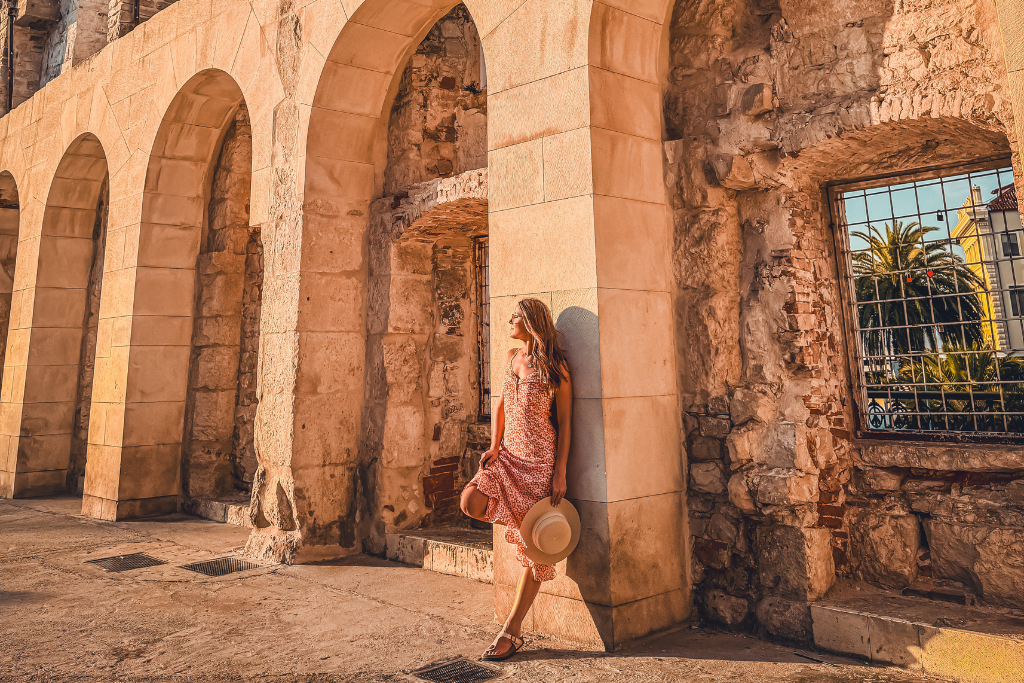Kate leaning against a wall soaking up the golden morning sunlight in a sundress.