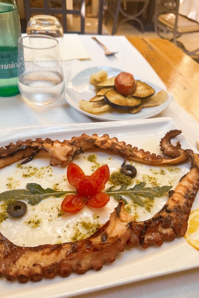 A plate of grilled octopus with vegetables and a glass of wine. 