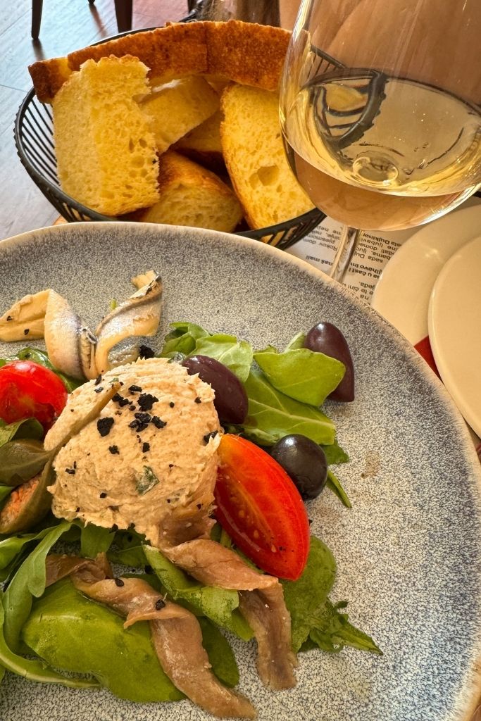 A glass of white Croatian wine next to a plate of sardine salad and bread.