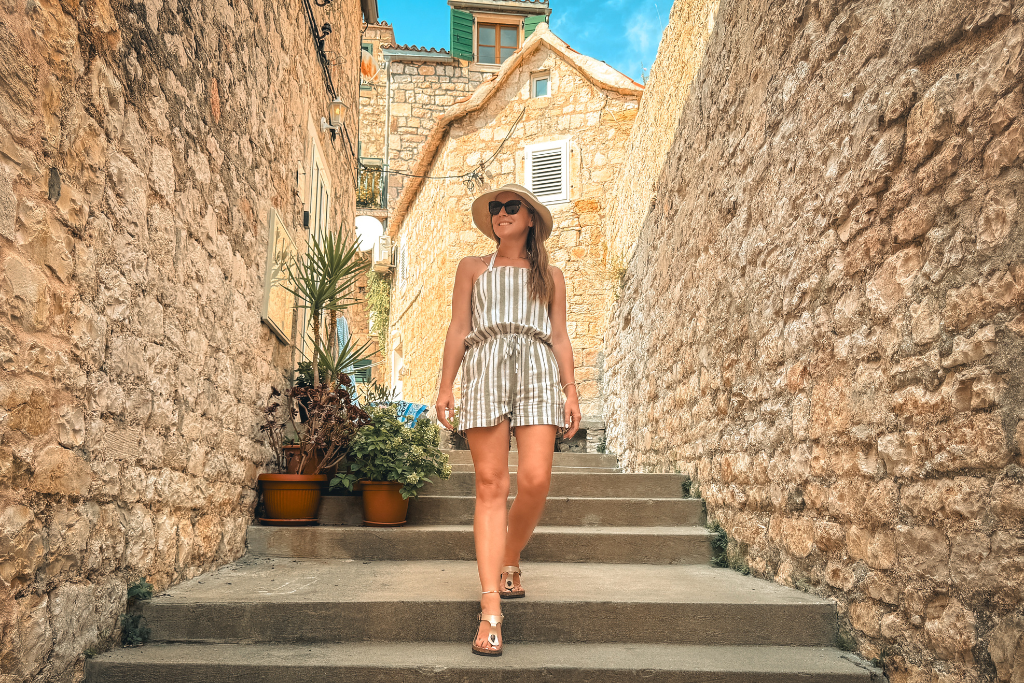 Kate is smiling as she walks down some stone steps in a narrow ally on the Island of Hvar in Croatia. 