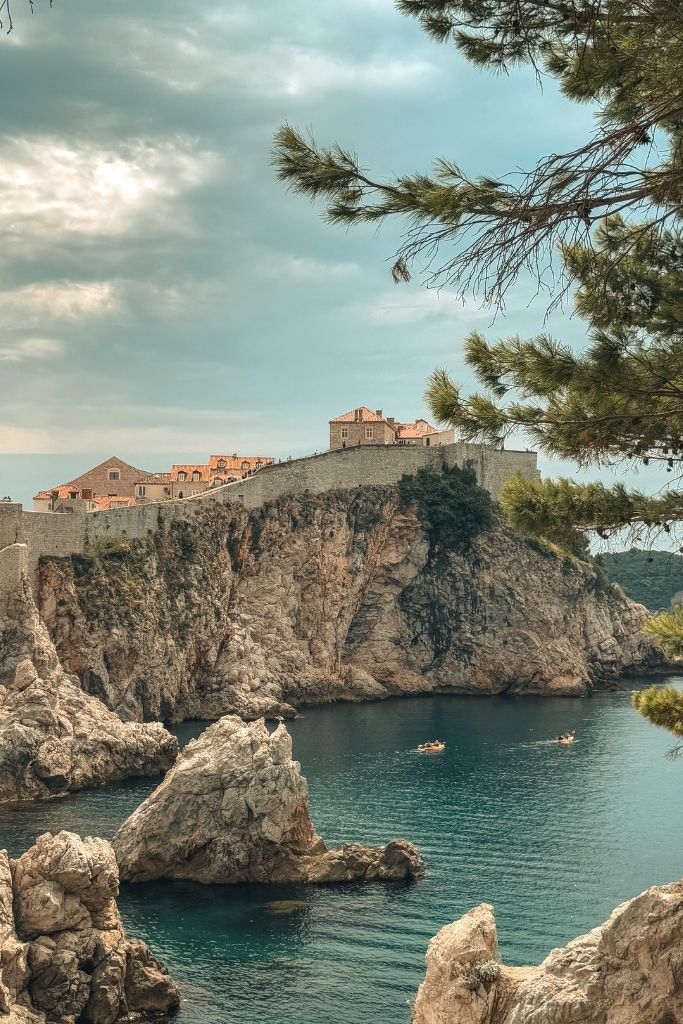 View of the rocky shore with sparkling blue water and the medieval stone wall of Dubrovnik, Croatia.
