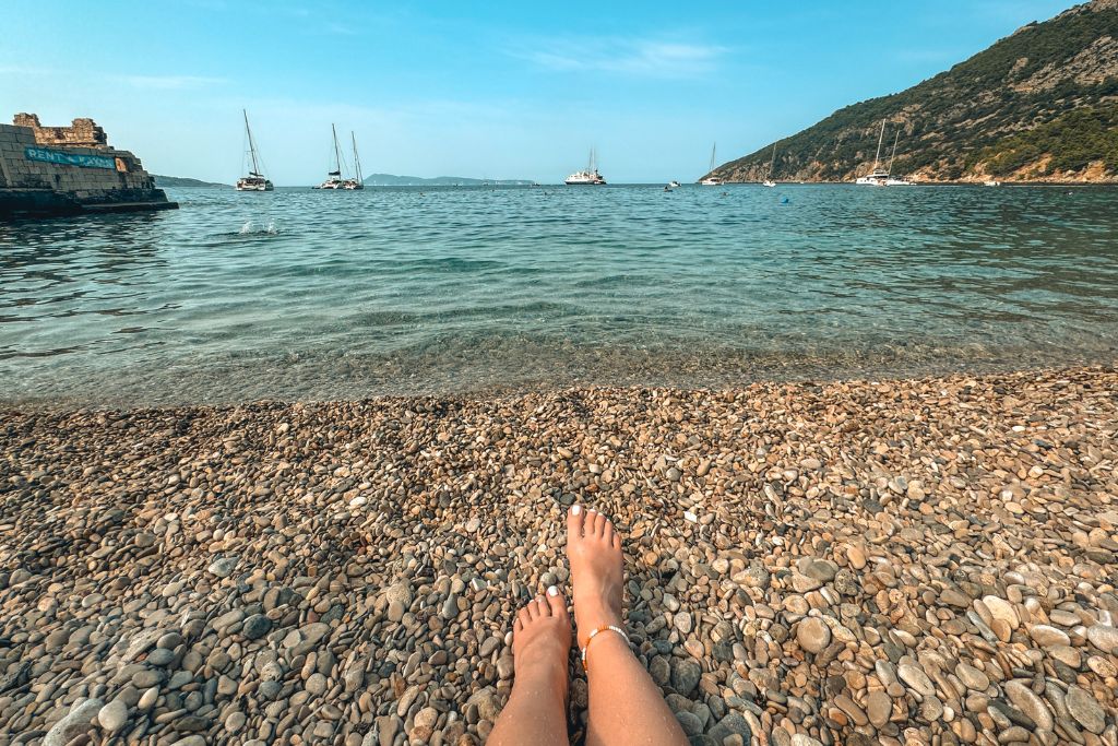 Kate laying on a pristine beach in Croatia looking out at the sailboats in the water off shore. 