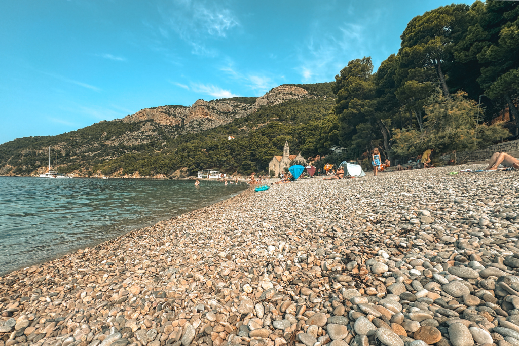 A close up view of a long beach covered in small pebbles with beach goers laying on the beach.