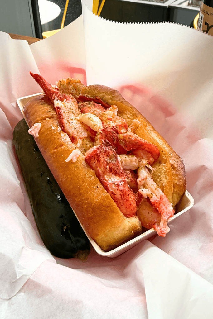 A fresh Lobster roll stuffed with juicy lobster meat and a pickle on the side. 