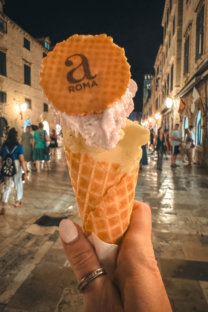 Kates handing holding a cone with two scoops of gelato at night in old town Dubrovnik.