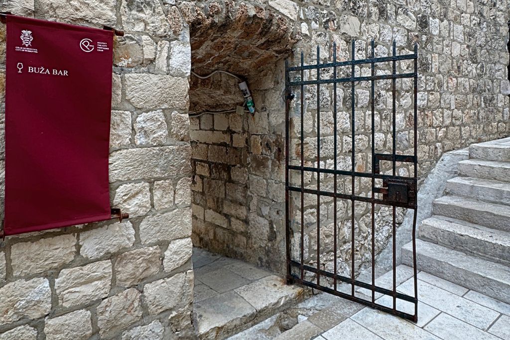 Man door with a gate and sign on a stone wall that says Buza Bar.