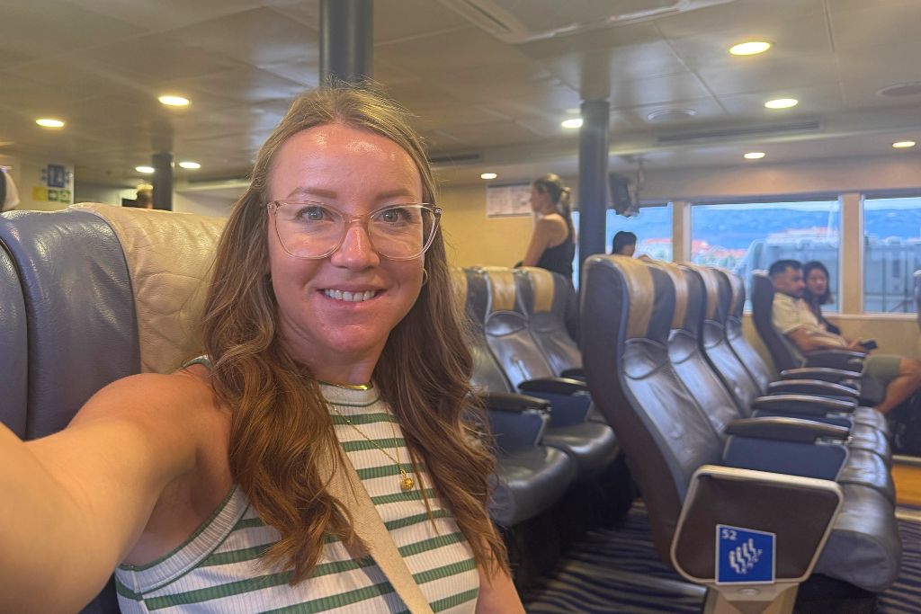 Kate smiling as she takes a selfie, sitting in her chair on a water ferry.