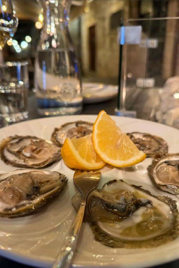 A plate of oysters with lemon wedges on a table under candlelight.