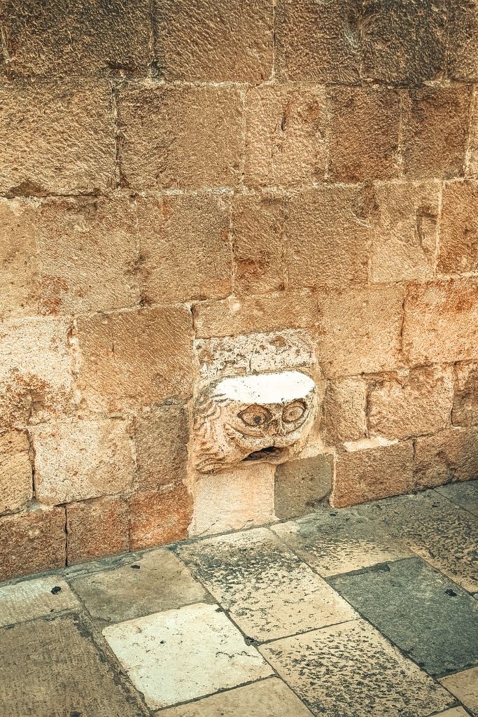 A stone jutting out of a stone wall with a face on it.