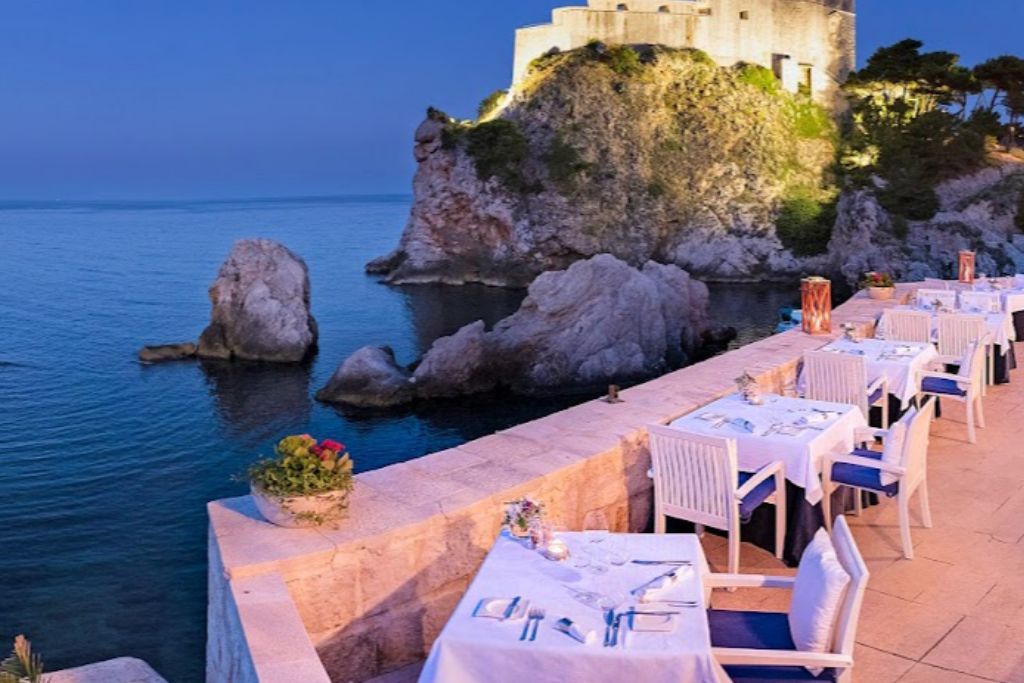 Evening setting of tables with white table cloths on  a terrace overlooking a sea view in Dubrovnik.