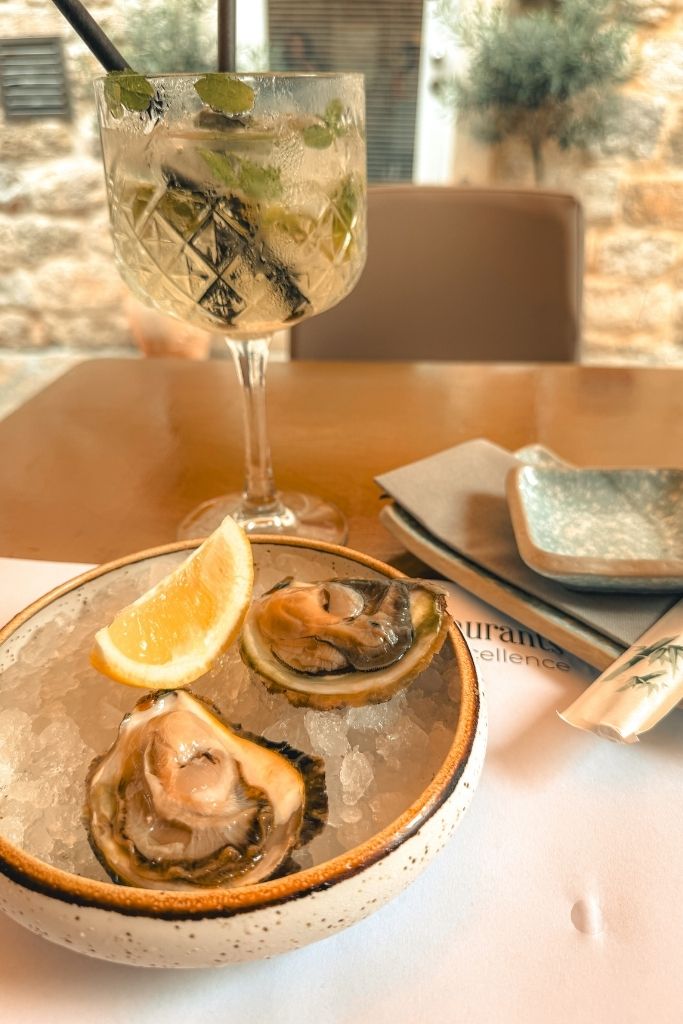 Table setting with a Hugo Spritz and a plate of oysters on ice with a slice of lemon.