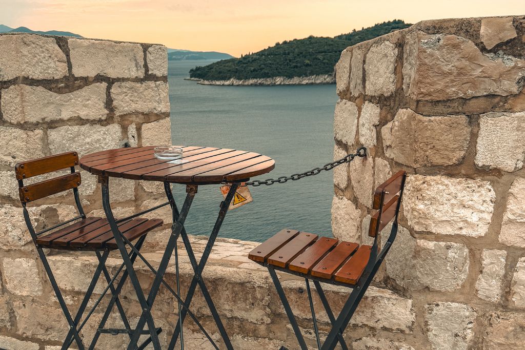 small table with two chairs set next to a stone wall with a view of Lokrum Island in the background.
