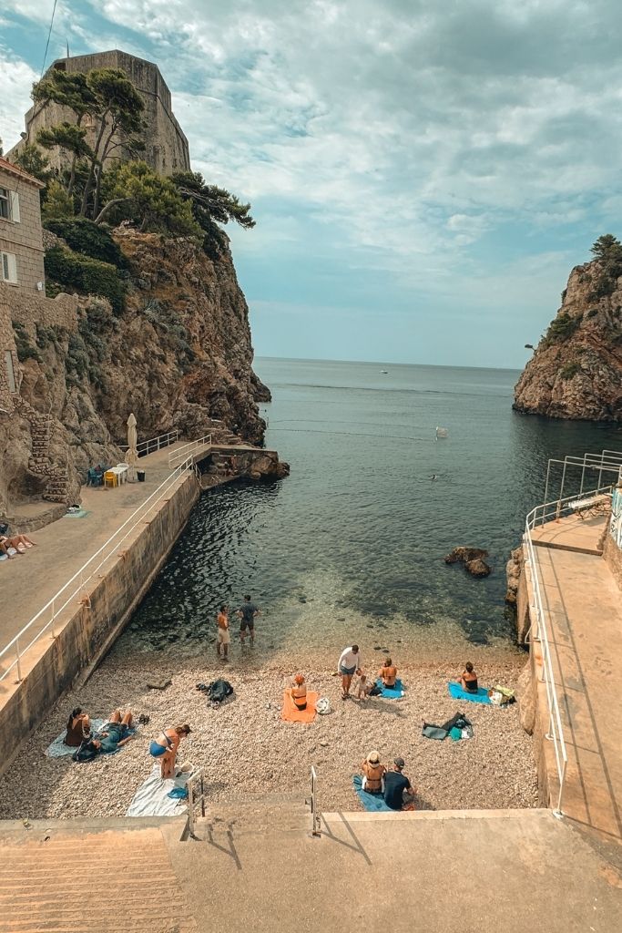 small beach tucked between towering cliffs with some beach goers laying on the beach.