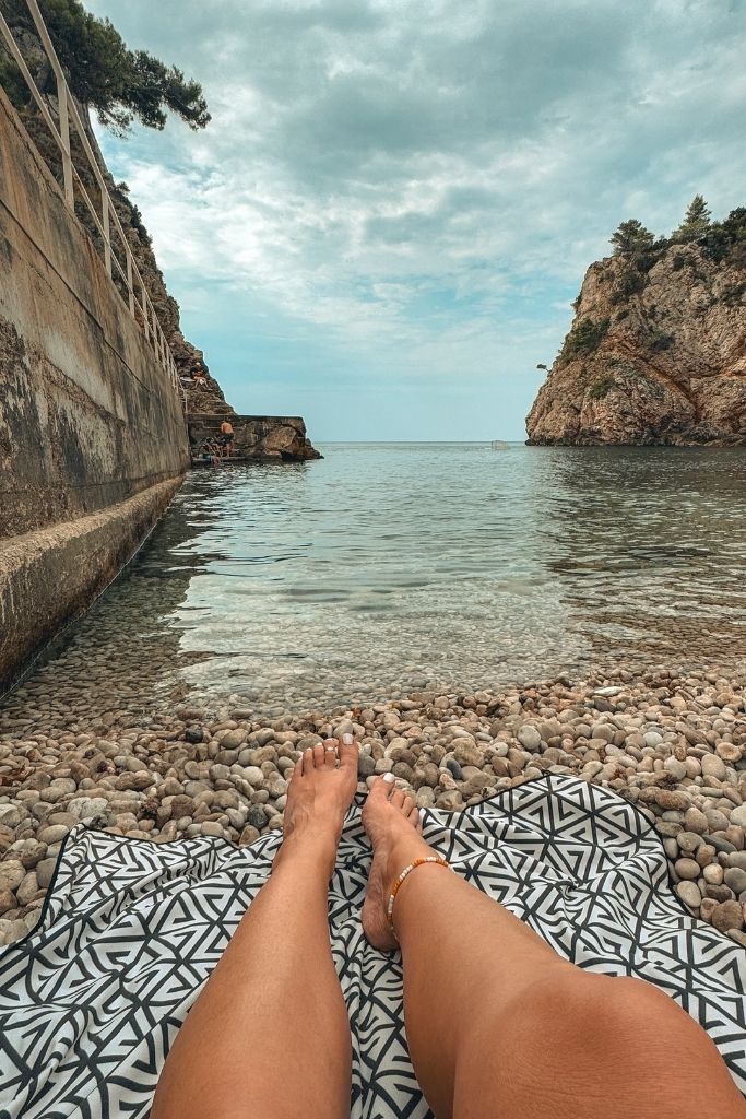 Kates legs stretched out toward the crystal clear water, laying on a beach towel.