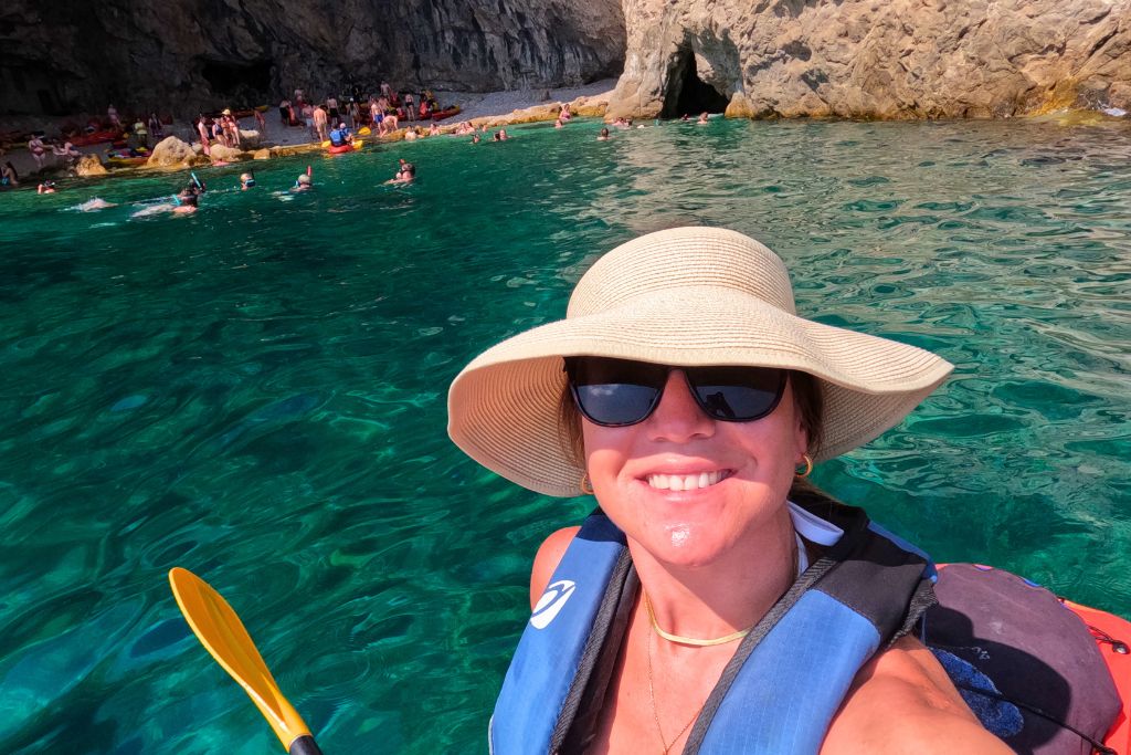 Kate taking a selfie from a kayak with a cave and turquoise water behind her.
