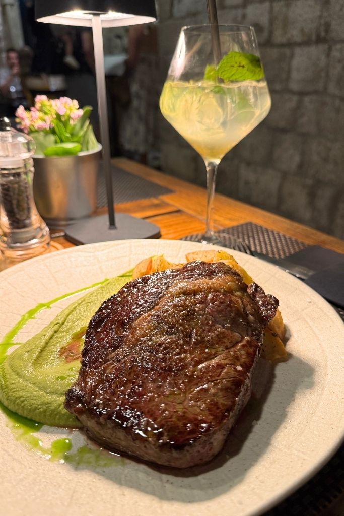 A juicy steak plated on a bed of asparagus puree with a Hugo Spritz.