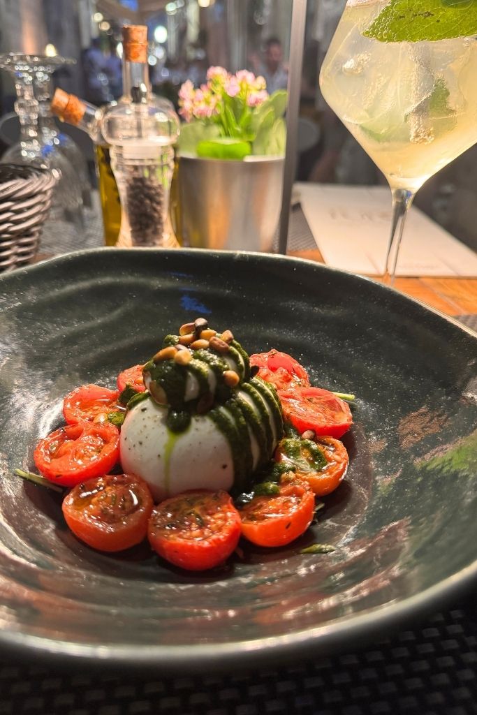 Caprese salad plated on a table with a Hugo spritz under candlelight.