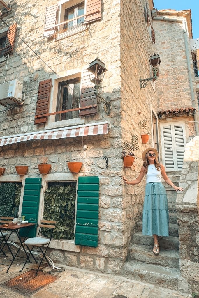 Kate walks down a set of steps along a historic stone building with turquoise shutters. 