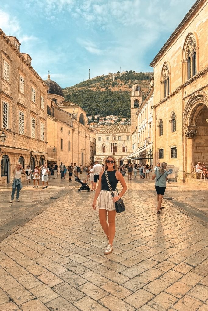 Kate standing in the middle of a polished marble road in Old Town Dubrovnik, wearing shorts and a tank top. 
