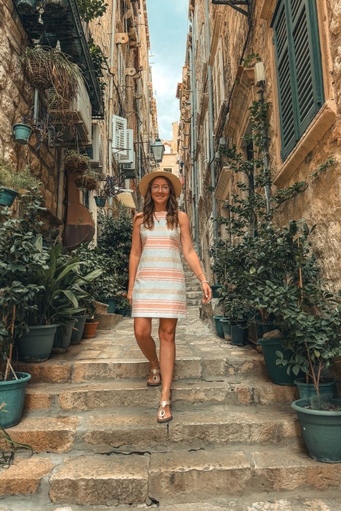 Kate walking down a flight of stairs lined with plants in a sun dress and sun hat.