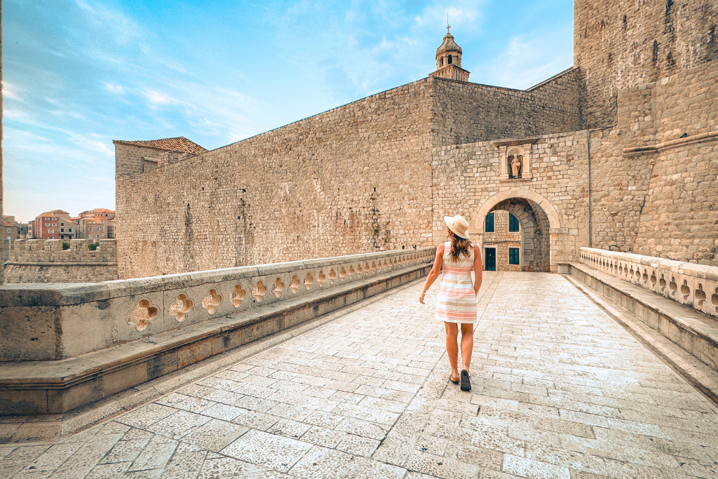 Kate is walking across a stone bridge, entering Dubrovnik's gate.