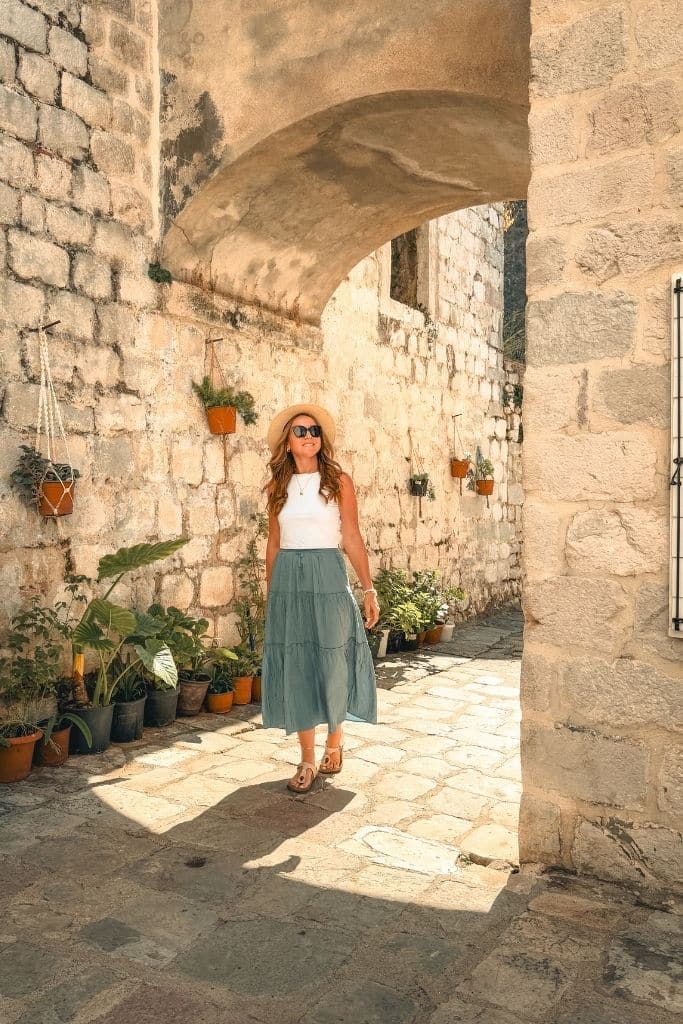Kate explores the charming stone alleyways of Kotor Old Town, surrounded by historic architecture and warm Mediterranean sunshine in Montenegro.