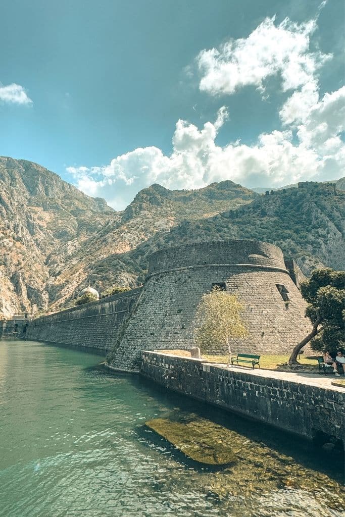 The ancient stone walls of Kotor stretch along the waterfront beneath Montenegro’s dramatic mountain landscape and crystal-clear bay waters.