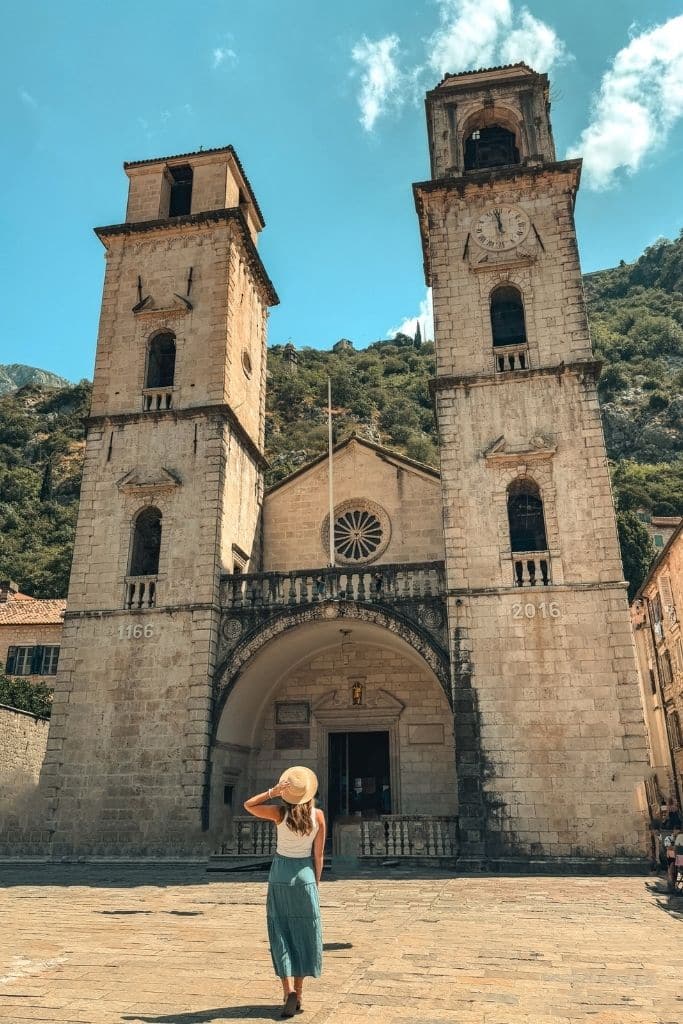 Kate stands beneath the iconic twin bell towers of Kotor Cathedral, surrounded by the dramatic mountain scenery and historic charm of Montenegro’s Old Town.