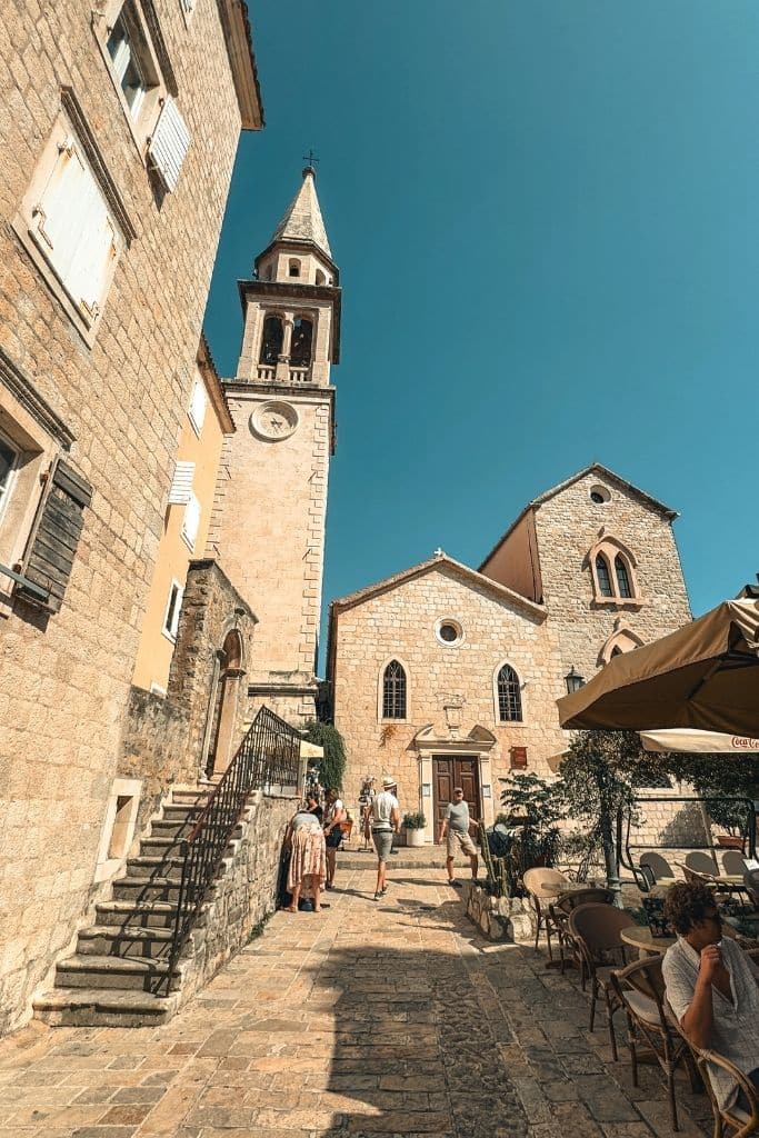 A charming stone church and bell tower rise above the cobblestone streets and outdoor cafes of Budva’s picturesque Old Town in Montenegro.