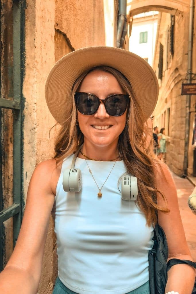 Kate explores the warm stone alleyways of Kotor Old Town wearing her portable neck fan — a total lifesaver during Montenegro’s hot summer days.
